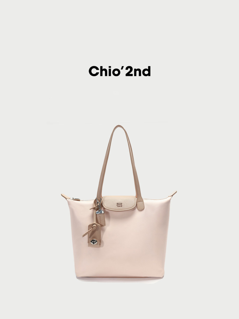 Light pink tote handbag with long handles and a front strap detail on a white background