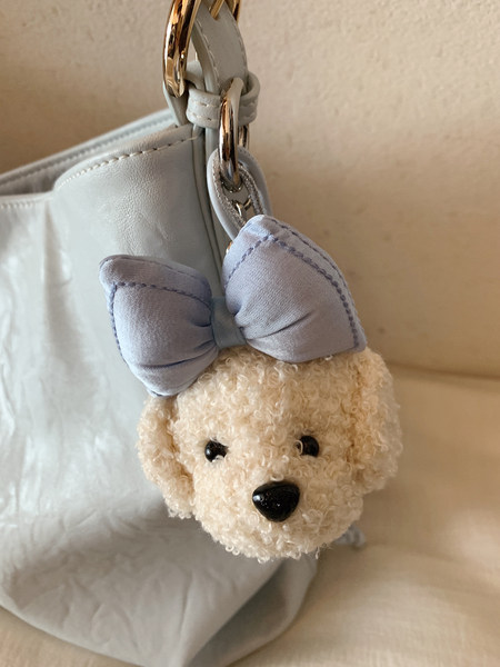 Plush teddy bear bag charm with a bow attached to a light blue handbag
