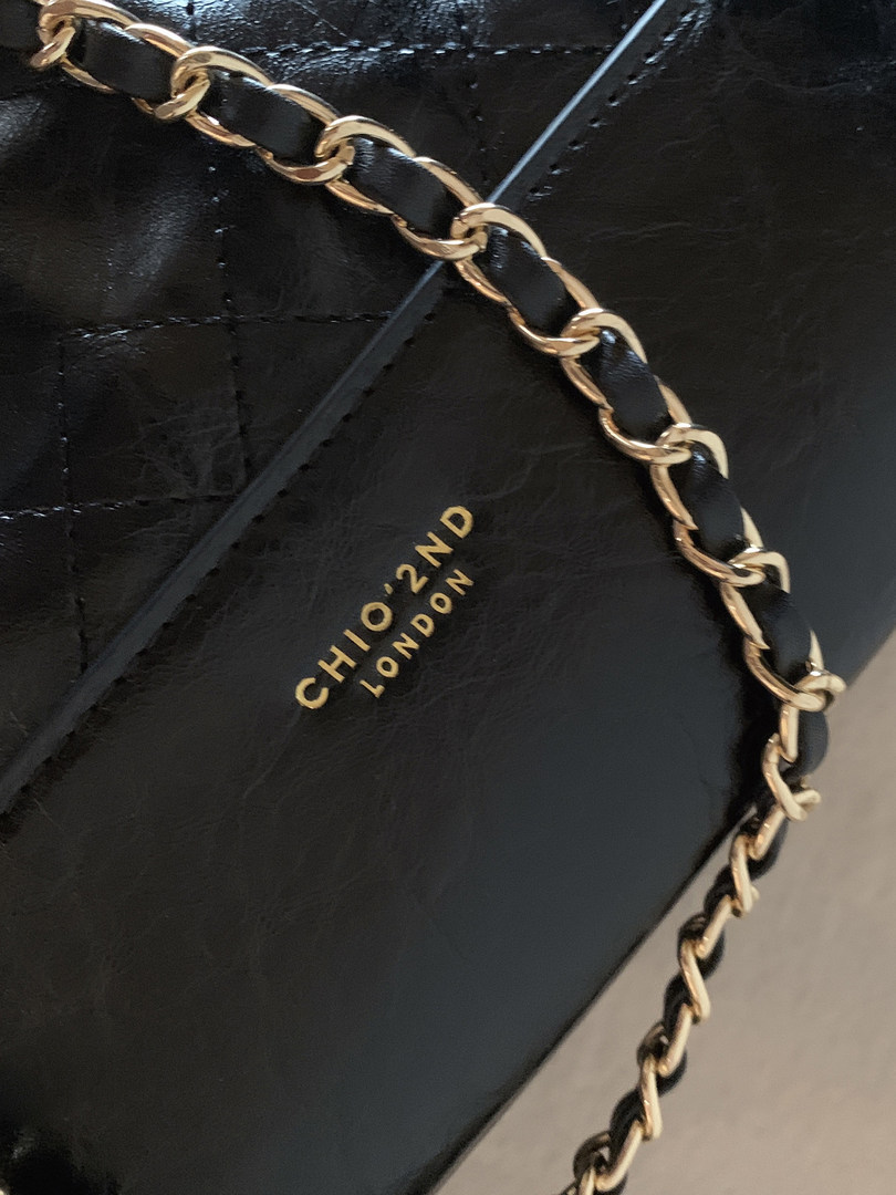 Close-up of a black leather chain-strap handbag with gold hardware and branding
