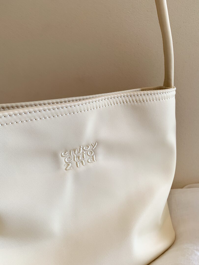 Cream shoulder bag with embroidered logo on a plain background