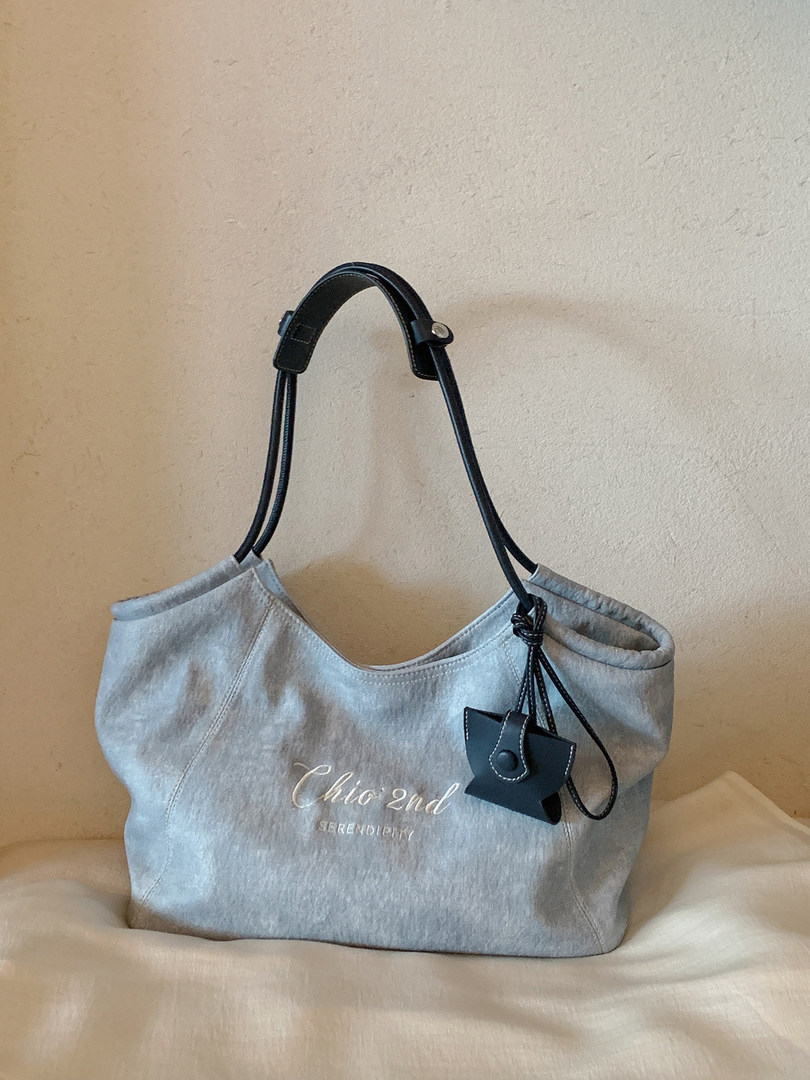 Light gray canvas tote bag with black handles and a small charm