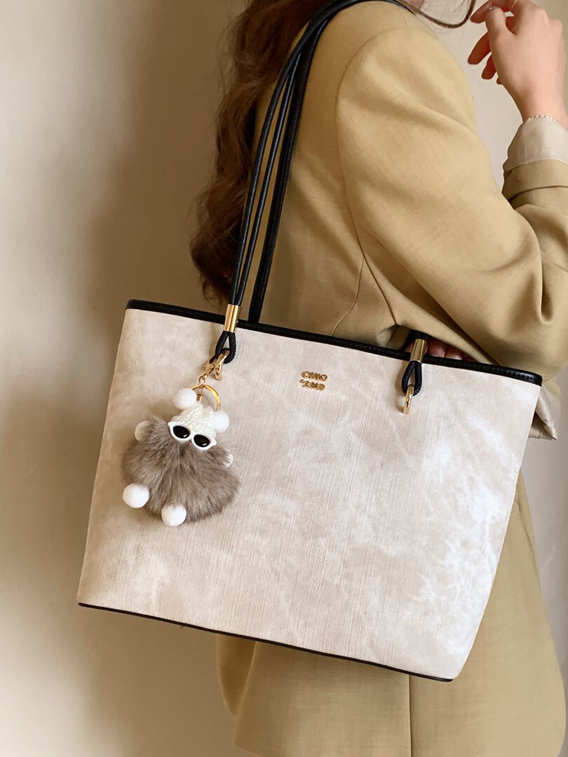 Beige tote handbag worn by a model with a fur charm
