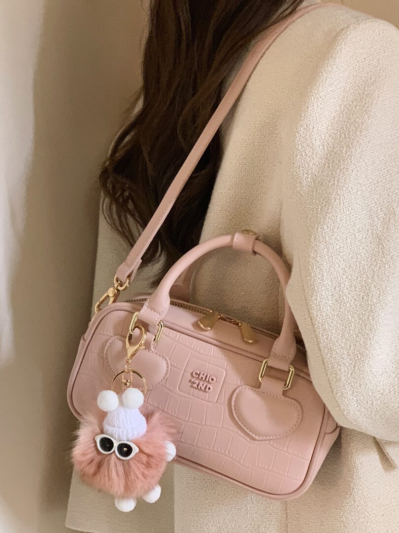 Pink structured handbag worn over the shoulder with a fuzzy charm
