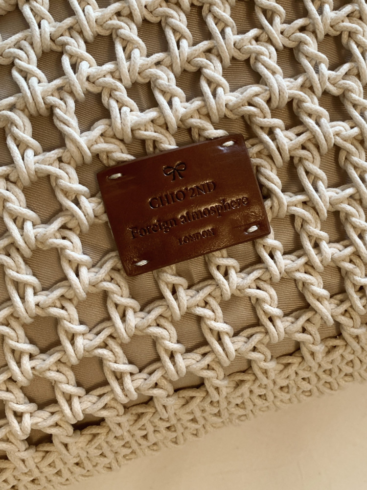 Close-up of a woven beige bag with a brown leather brand label.
