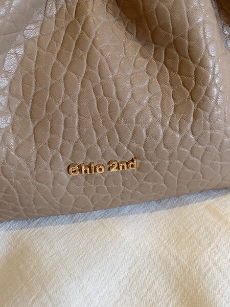 Close-up of a beige textured leather bag with gold logo lettering