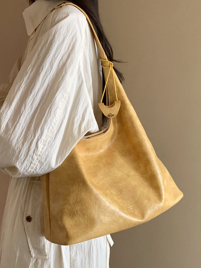 Mustard yellow leather tote bag worn over a white outfit
