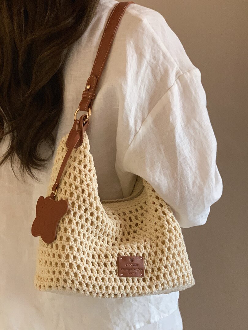 Crocheted cream shoulder bag with brown leather strap worn on a model