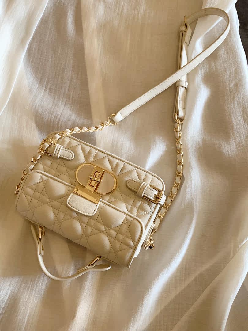 Cream quilted mini handbag with gold chain strap on fabric background
