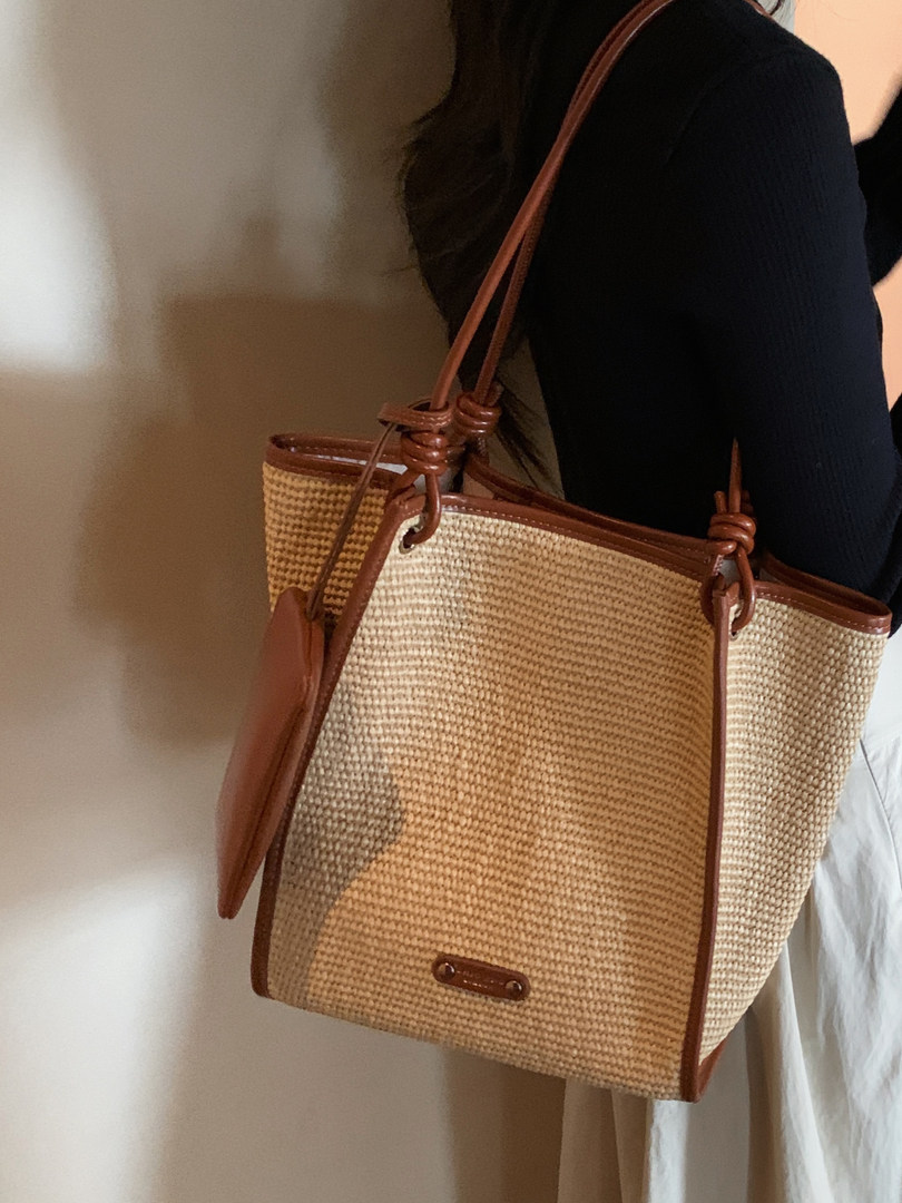 Woven straw tote bag with brown leather trim being carried