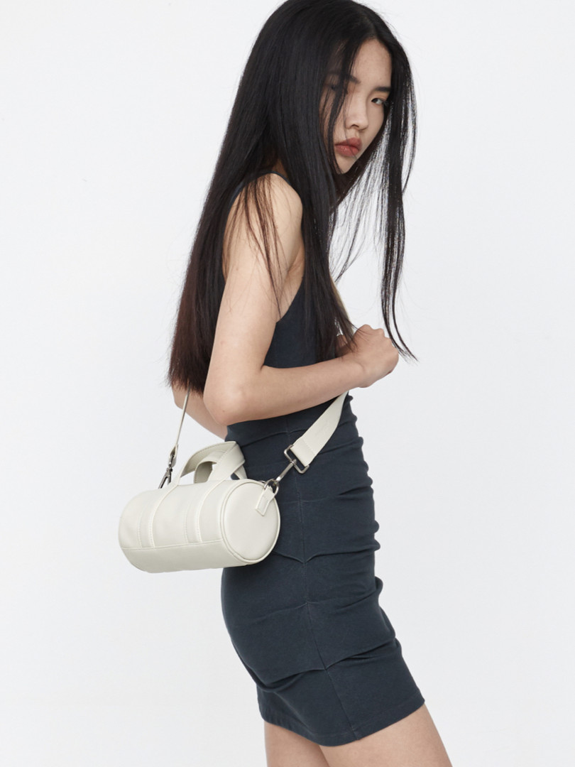 White cylindrical crossbody handbag worn by a model on a plain background