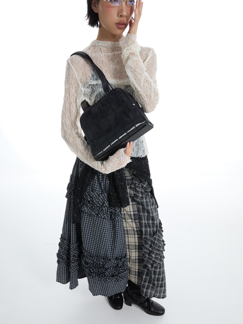 Model wearing a black shoulder bag with a layered textured outfit on a white background