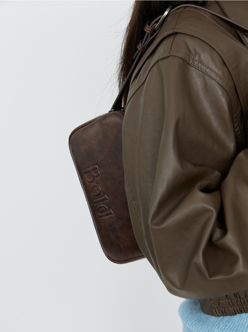 Brown leather shoulder bag worn by a model with an olive jacket