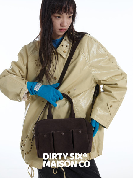 Model wearing an oversized beige jacket and carrying a dark shoulder bag