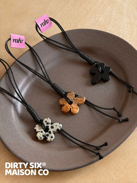 Flat lay of black cord flower pendant necklaces with assorted stone charms on a plate.