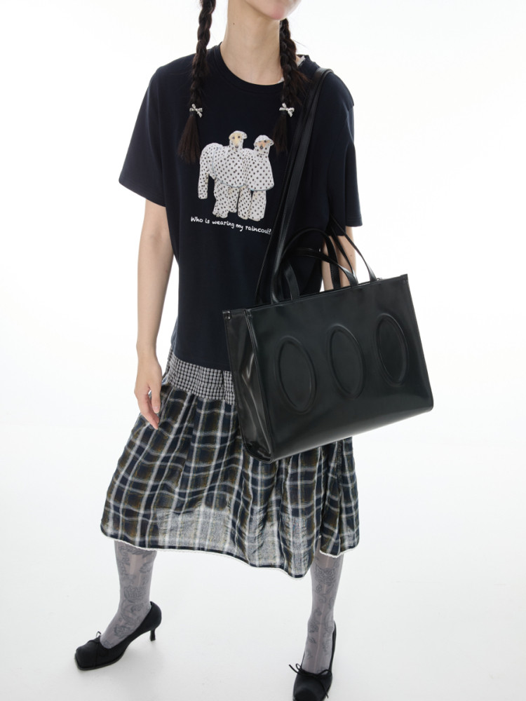 Model wearing a black graphic T-shirt, plaid skirt, and black tote bag