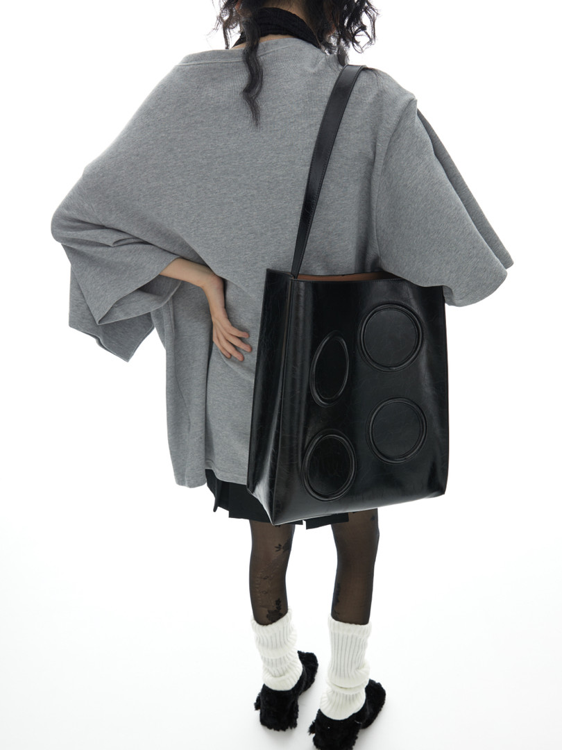 Black leather shoulder tote bag worn by a model with an oversized gray top