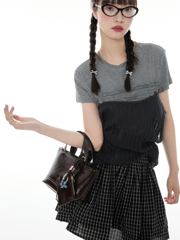 Model wearing a layered gray and black outfit with a small dark handbag