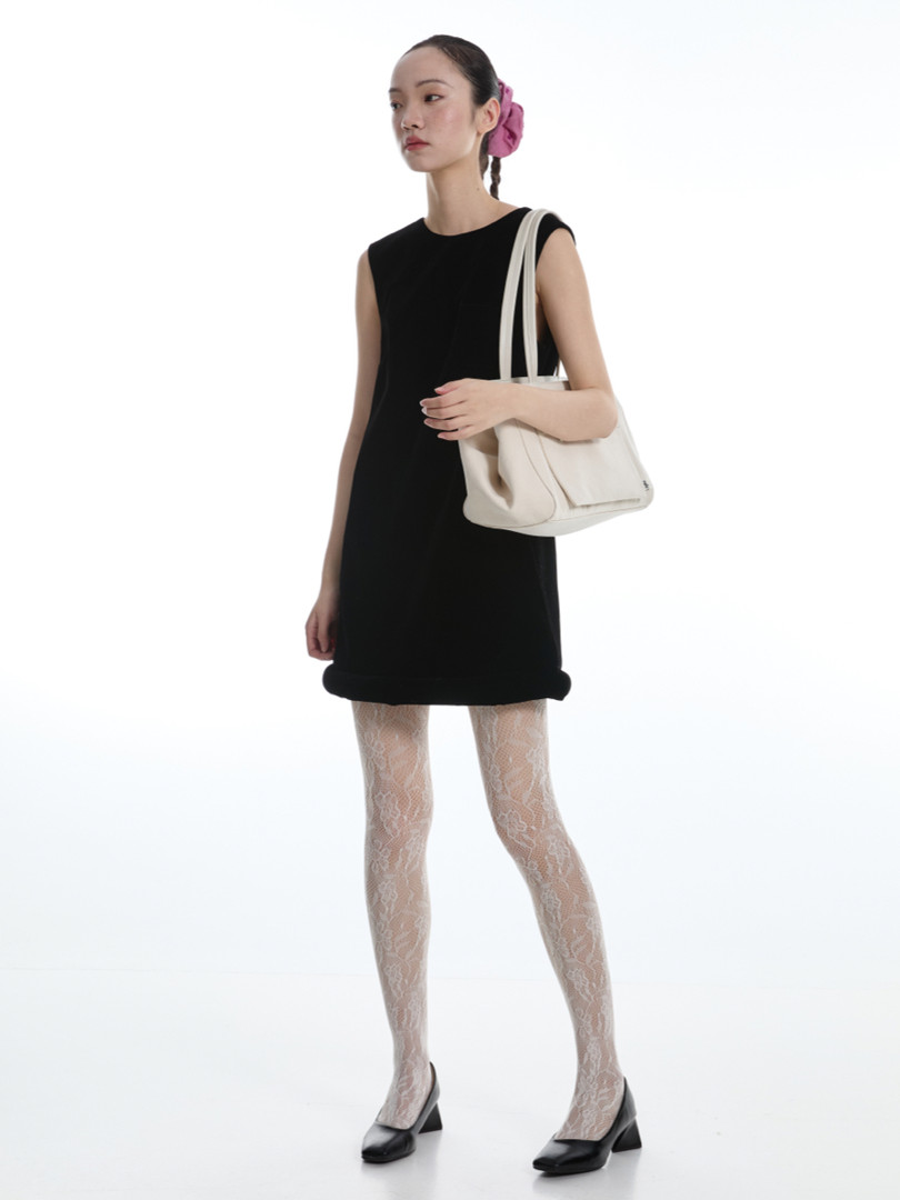 Black sleeveless dress worn by a model with a white handbag and heels