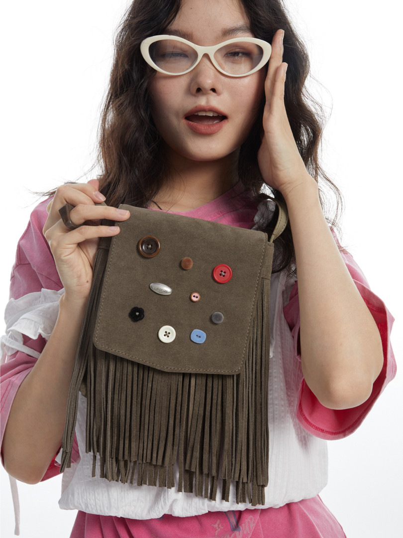 Fringed olive-brown crossbody handbag held by a model