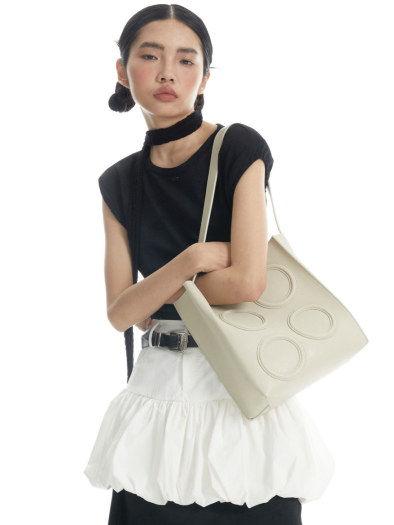 Model wearing a black sleeveless top and white skirt with a beige tote bag