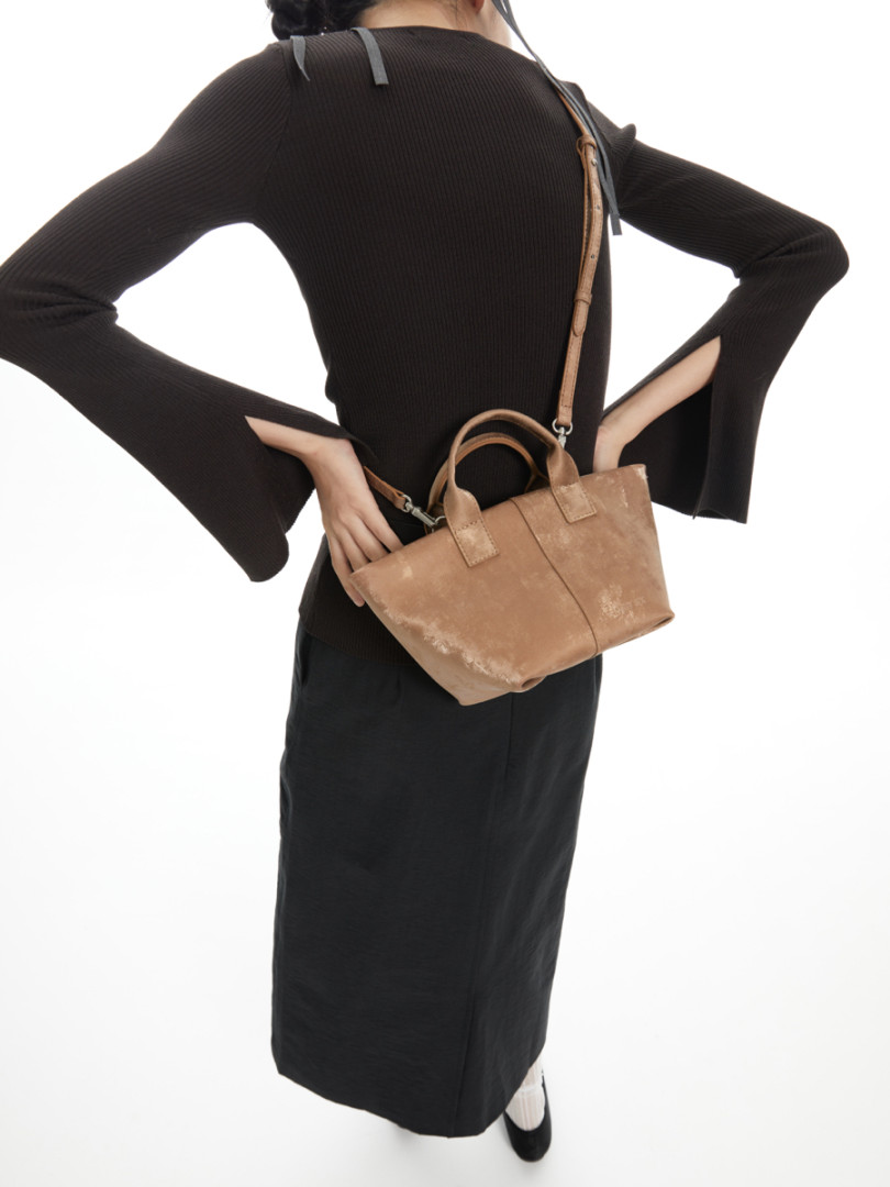 Model wearing a black outfit with a tan leather handbag