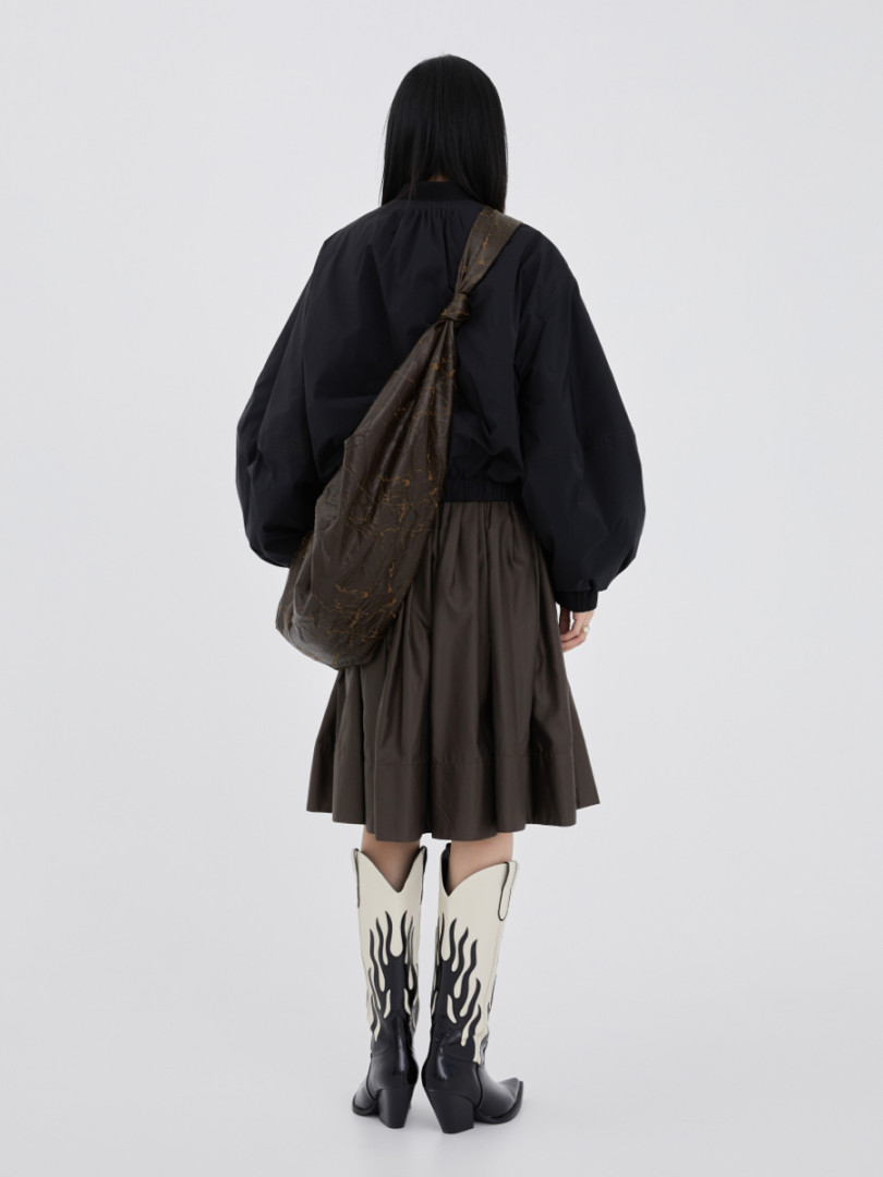 Fashion model wearing a black top, brown skirt, and flame-print knee-high boots with a slouchy shoulder bag