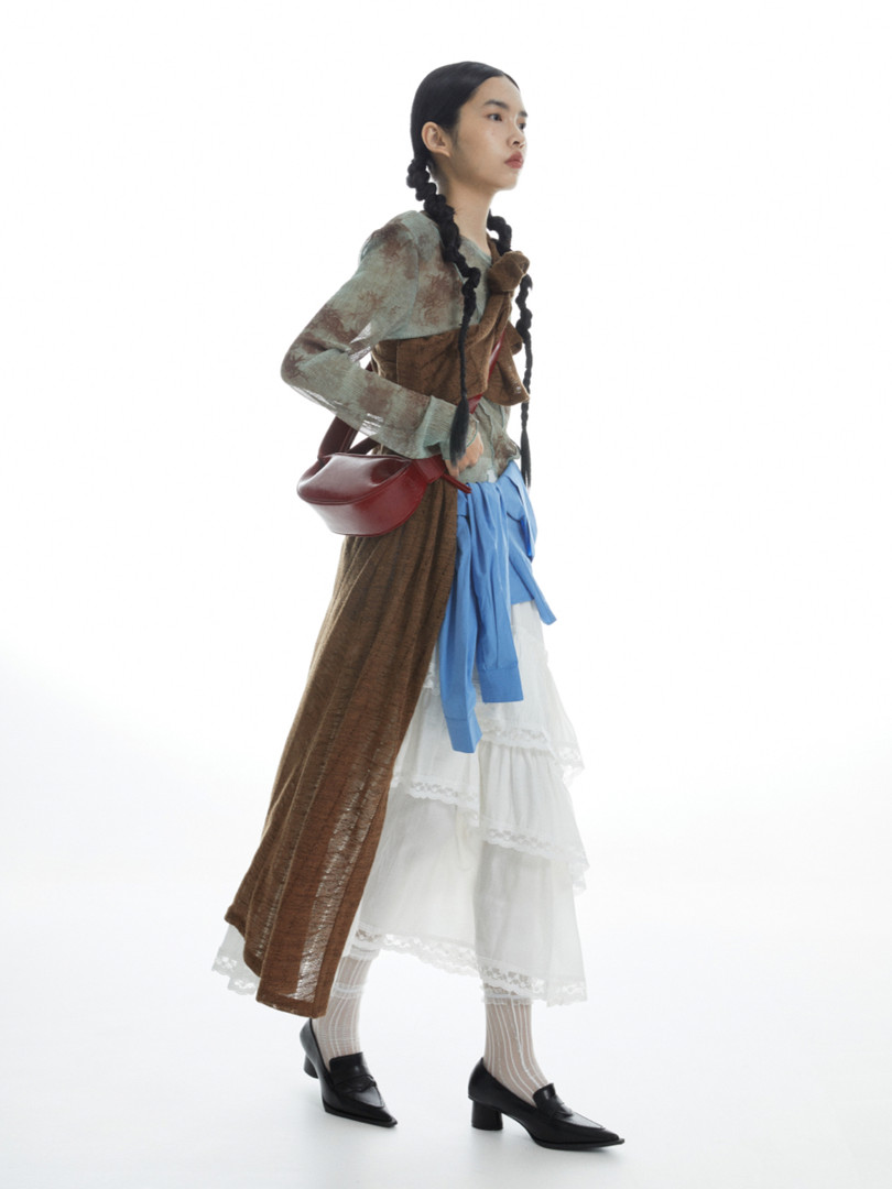 Fashion model wearing a layered vintage-style outfit with a red shoulder bag and black heels
