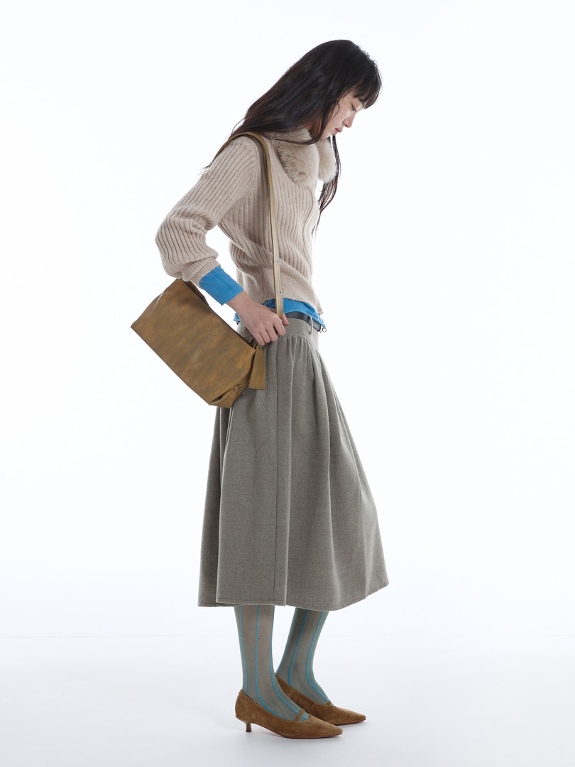 Model wearing a beige knit sweater, gray skirt, tights, heels, and a brown shoulder bag