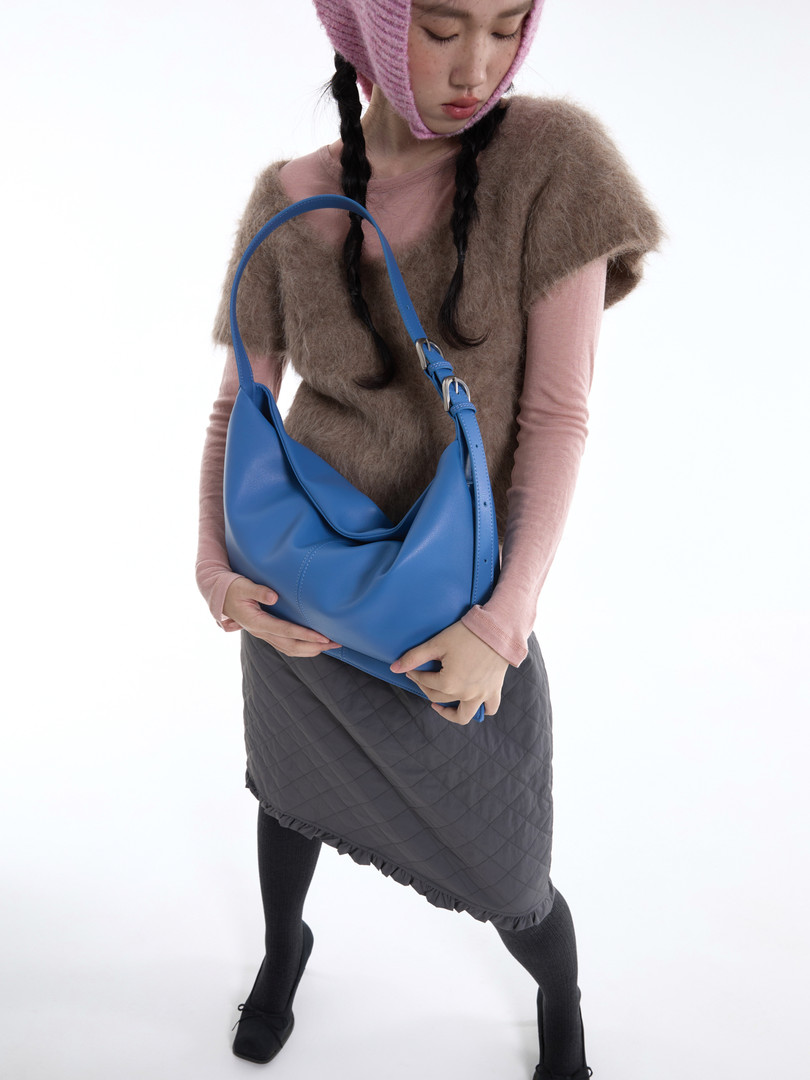 Model holding a blue leather shoulder bag.