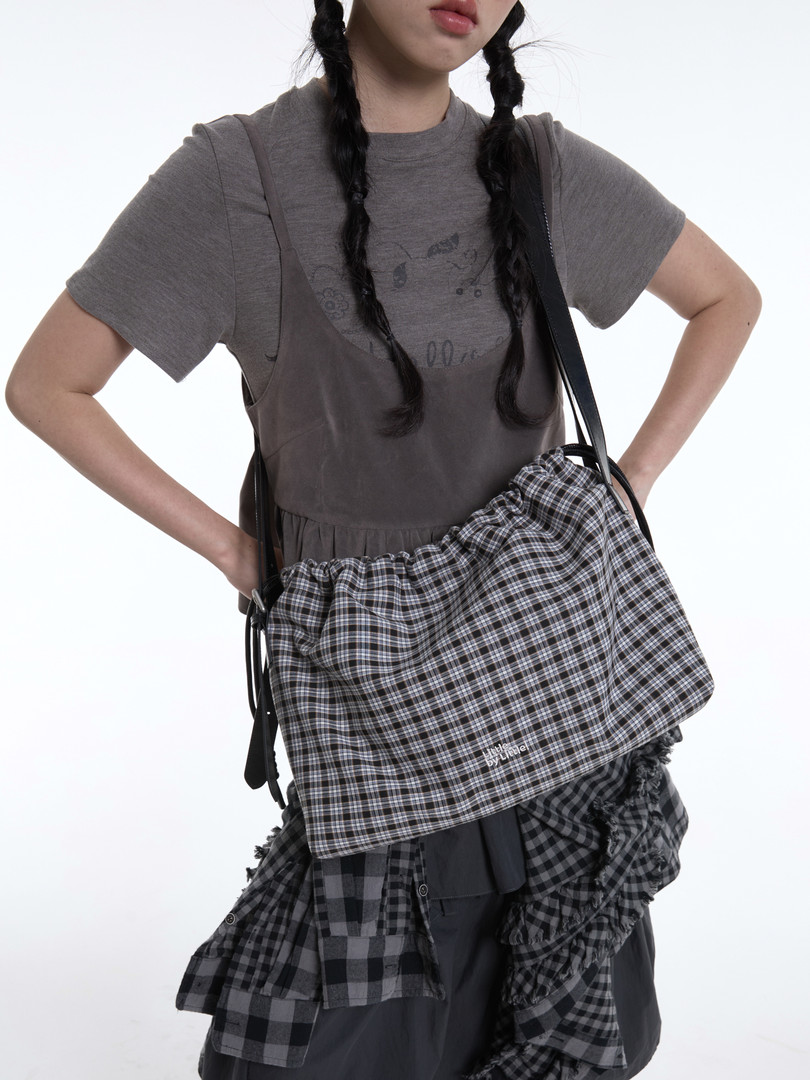 Model wearing layered gray outfit with a plaid drawstring shoulder bag