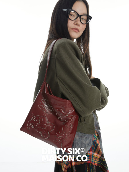 Model wearing a burgundy shoulder bag with decorative stud detailing