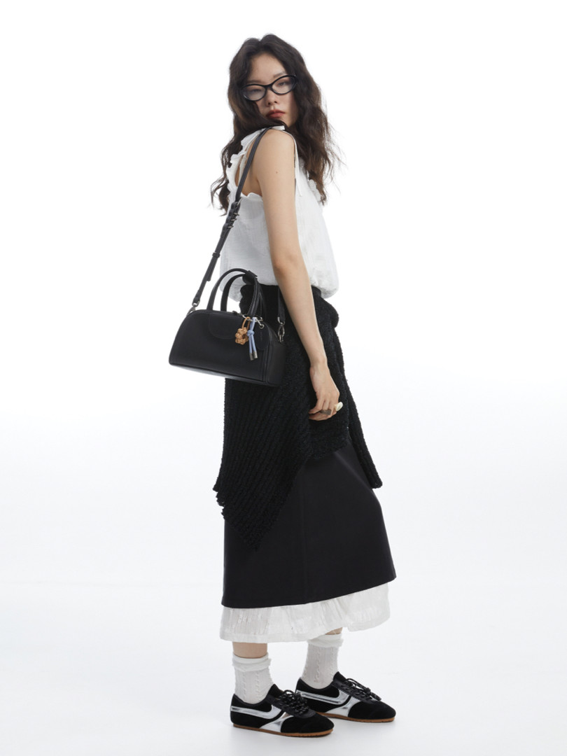 Model wearing a white sleeveless top with black skirt, black handbag, and sneakers