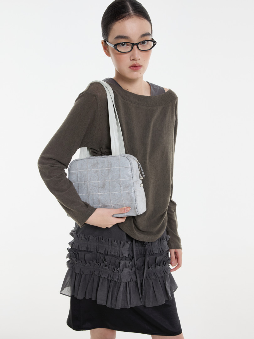 Model wearing a dark long-sleeve outfit and holding a light gray shoulder bag
