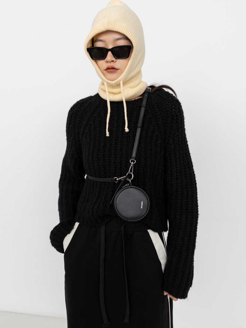 Model wearing a cream knit balaclava, black sweater, and round crossbody bag
