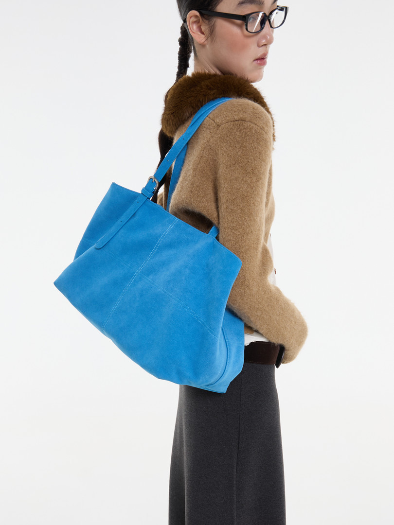 Model wearing a bright blue tote bag over a brown coat