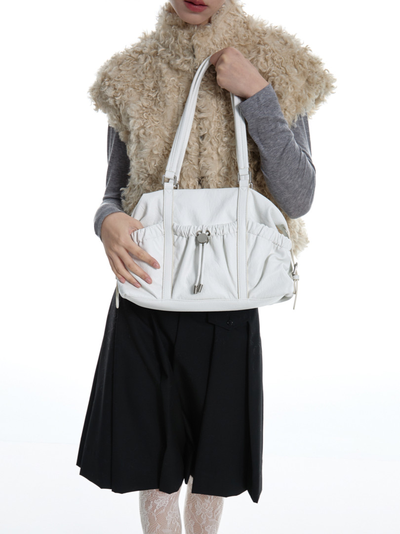 White shoulder handbag held by a model on a plain background