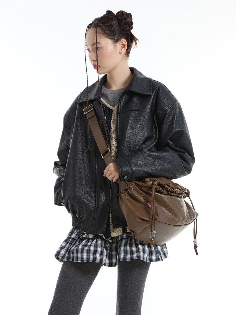 Model wearing a black faux leather jacket with a brown shoulder bag and plaid skirt