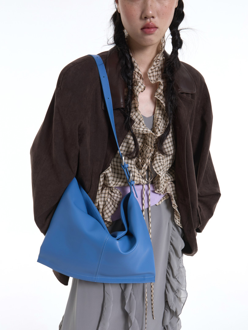 Blue shoulder bag worn by a model with layered fashion outfit