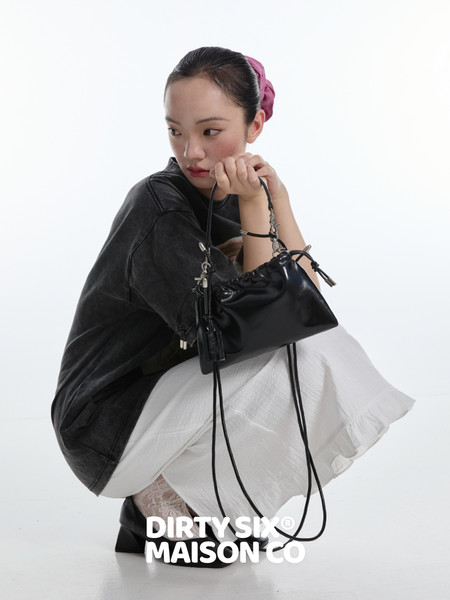 Black handbag held by a seated model on a white background