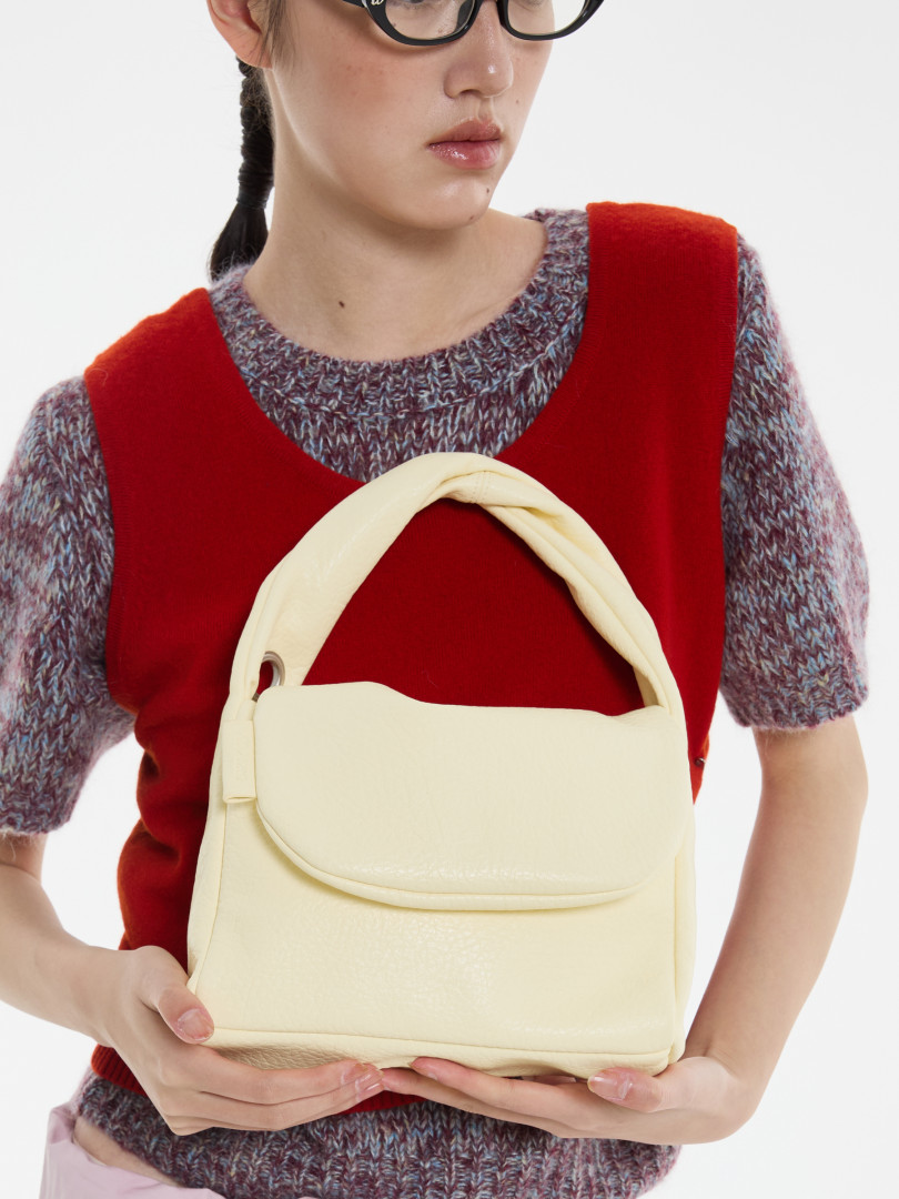 Cream-colored handbag held by a model wearing a red top and knit sweater