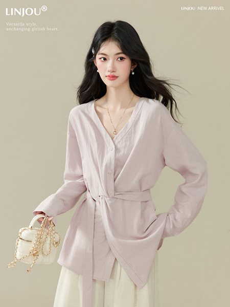Model wearing a light pink wrap-style blouse with a white handbag