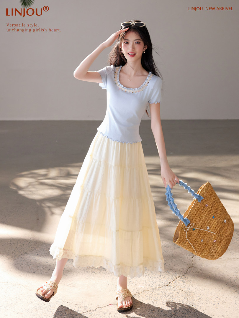 Model wearing a light blue top with a cream maxi skirt and straw bag