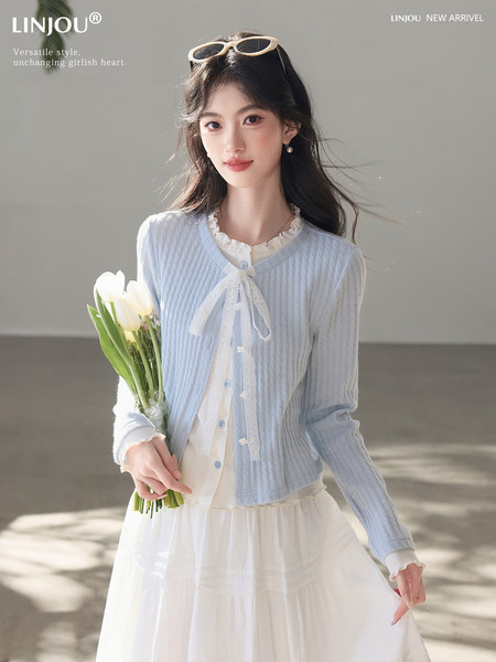 Woman wearing a light blue cardigan over a white dress, holding flowers