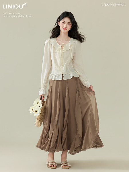 Model wearing a cream blouse and brown flowing skirt with a woven bag