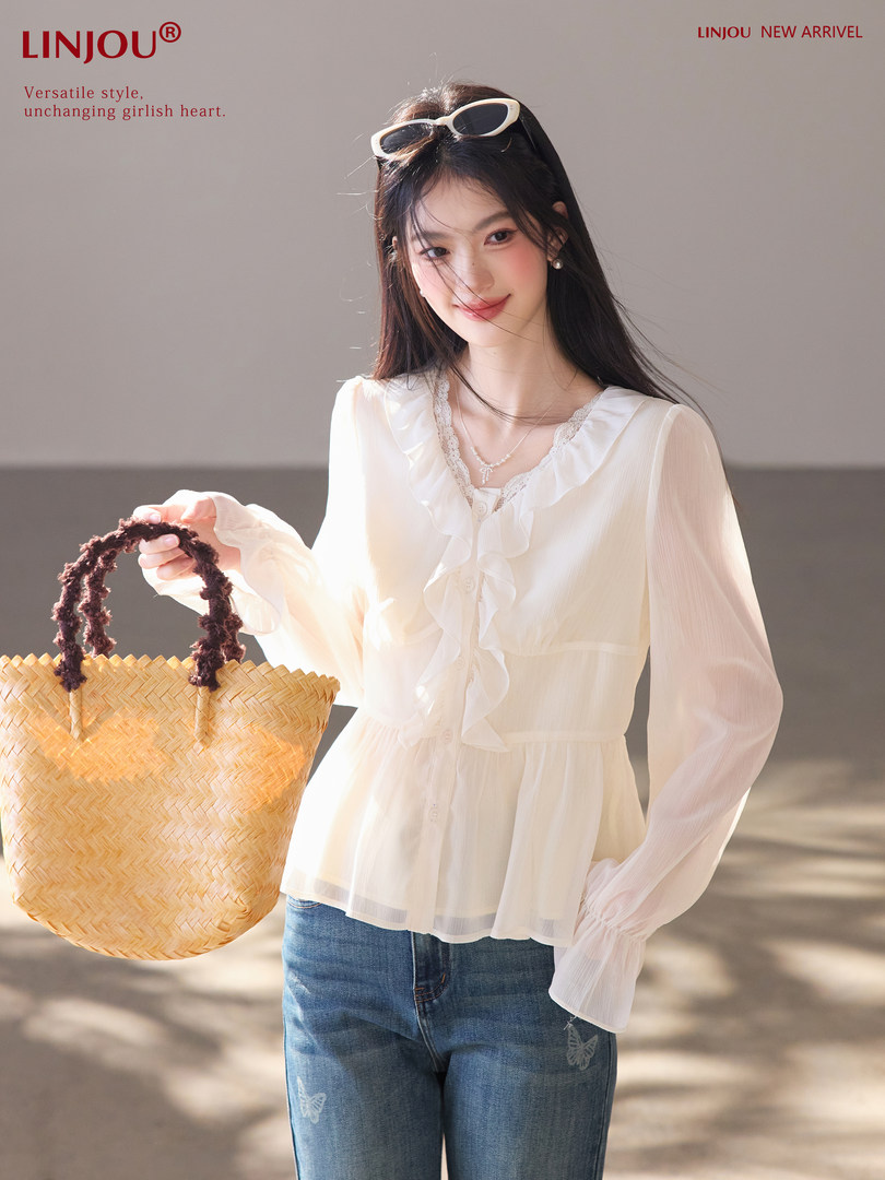 Model wearing a white ruffled sheer blouse with jeans and a straw tote bag
