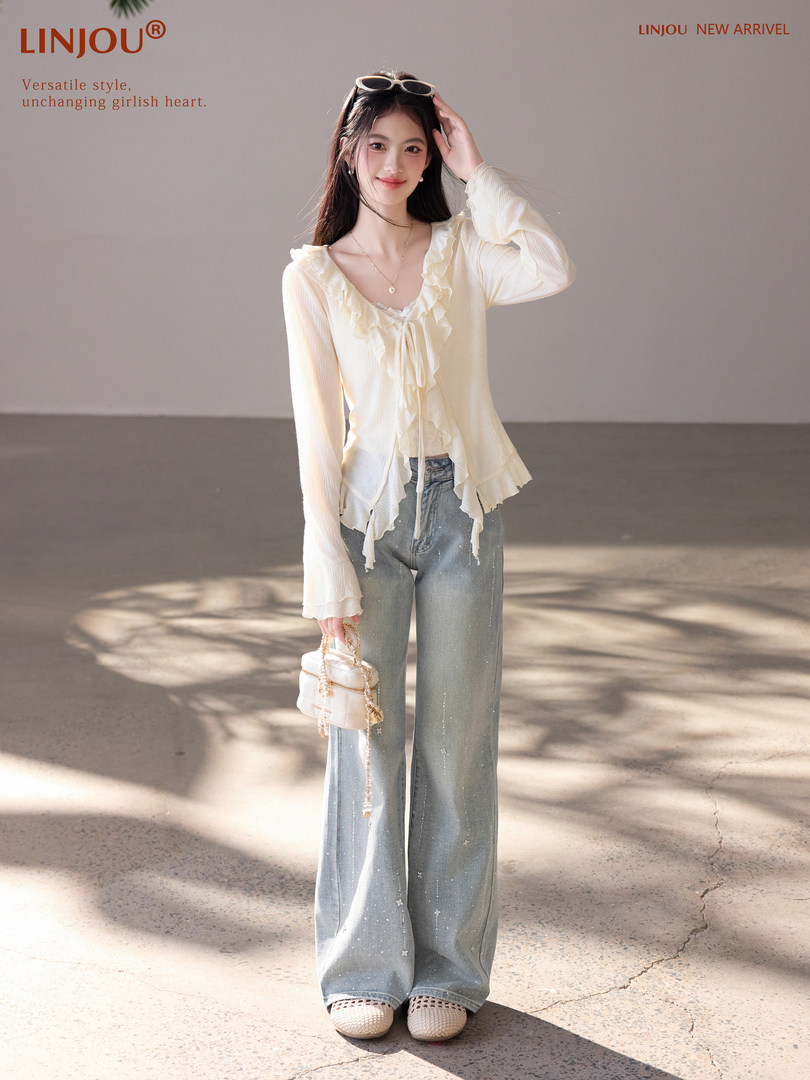 Model wearing a cream ruffled long-sleeve top with wide-leg jeans and a small handbag