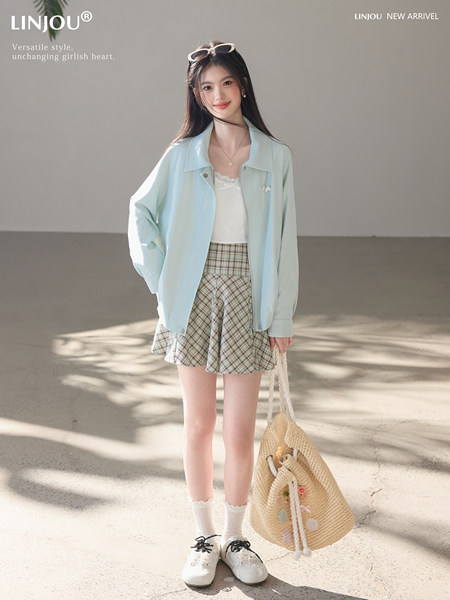 Young woman wearing a pastel light blue jacket with plaid skirt, holding a straw tote bag