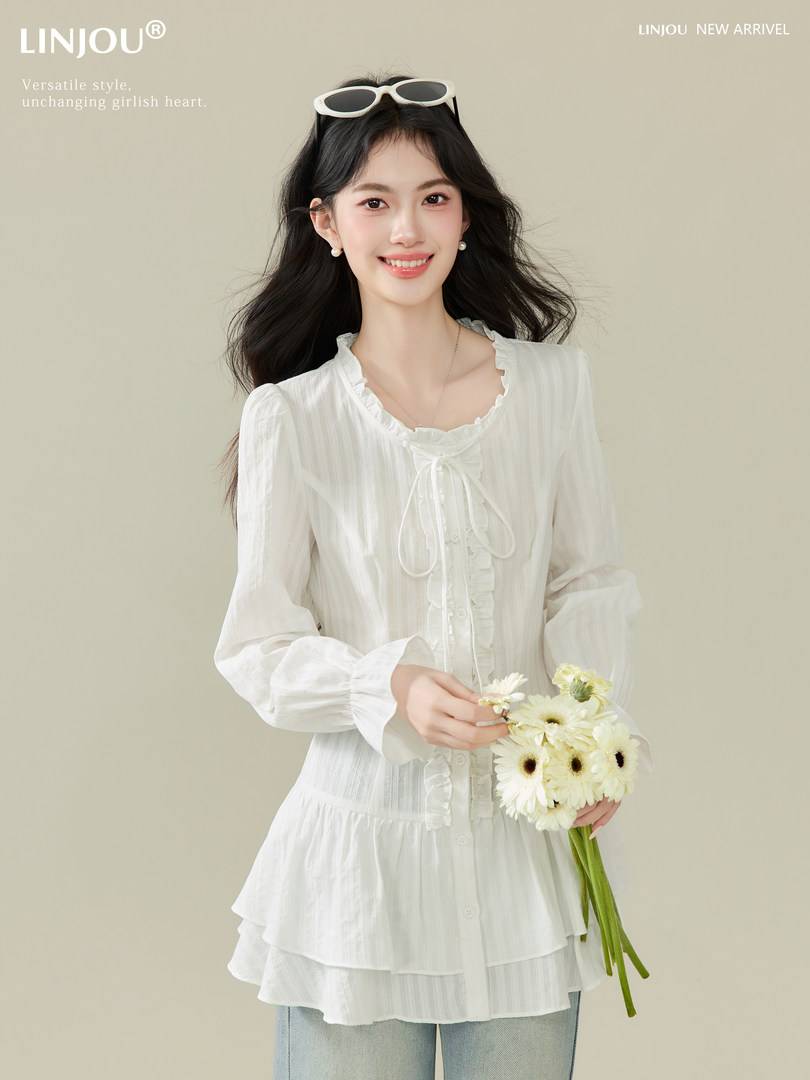 Model wearing a white ruffled long-sleeve blouse with a tie front