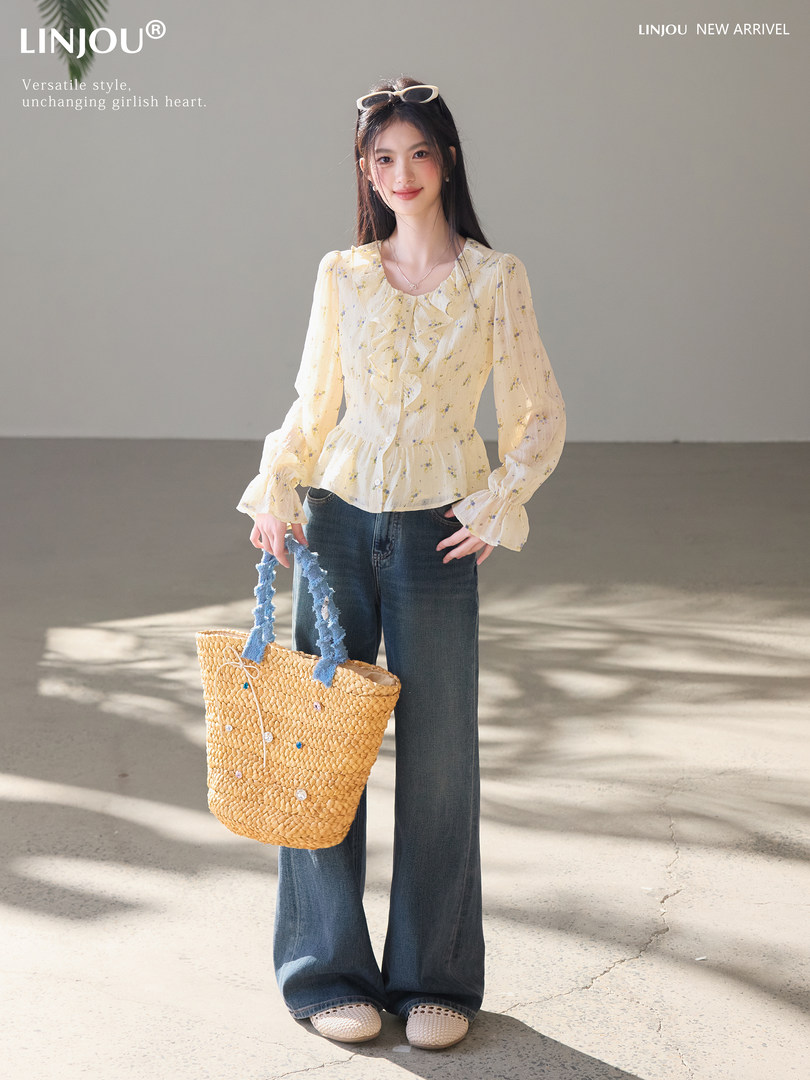 Model wearing a pale yellow floral blouse with wide-leg jeans and a woven tote bag