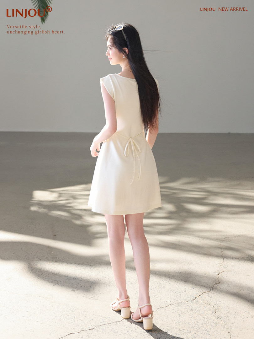 Woman wearing a light cream sleeveless dress with a tied waist